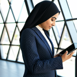 A professional Arab female entrepreneur, in a modest business suit, confidently analyzing digital marketing data on a sleek tablet in a modern, sunlit co-working space with subtle Islamic geometric patterns in the background. She is fully clothed, appropriate attire, safe for work, perfect anatomy, well-formed hands, natural proportions, professional photography, high quality.